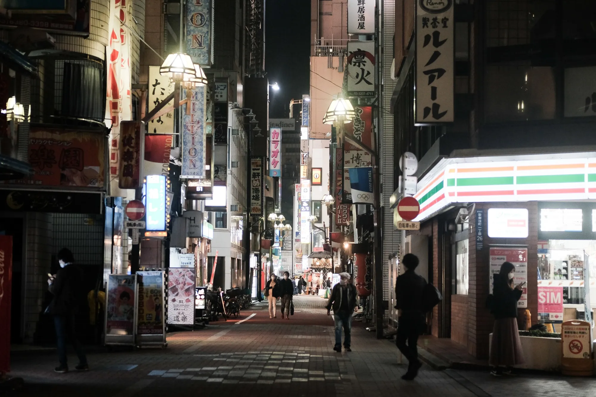 People walk among bars on a street at night in the Shinjuku district of Tokyo.