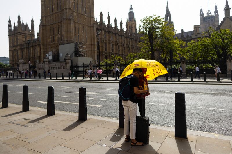 A tourist speaks with a tour guide under the shade of an umbrella, near the Houses of Parliament, during hot weather, in London, UK, on Wednesday, Sept. 6, 2023. 