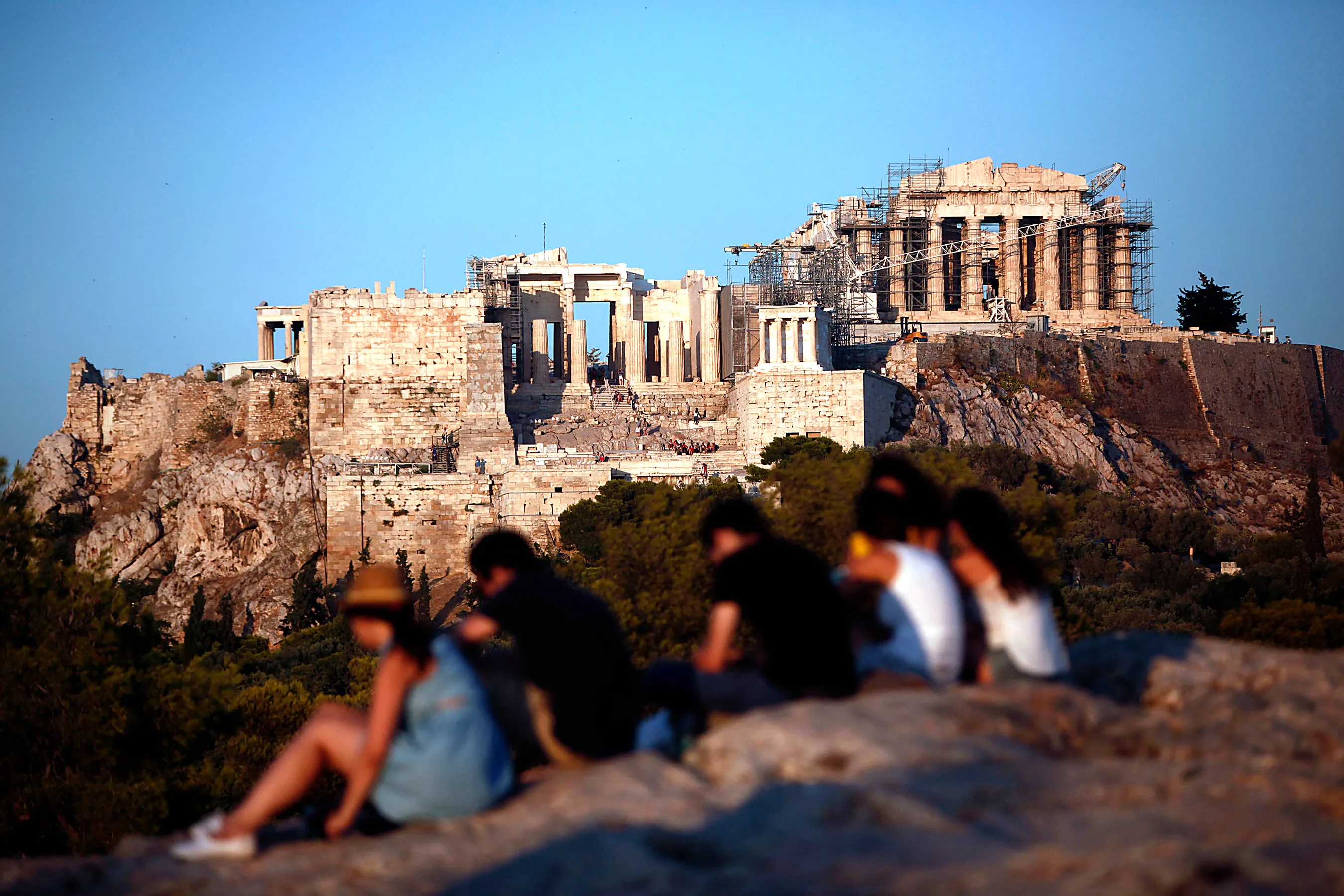 Tourists sit on rocks with a view of the Parthenon temple in Athens. Photograph by Angelos Tzortzinis/Bloomberg