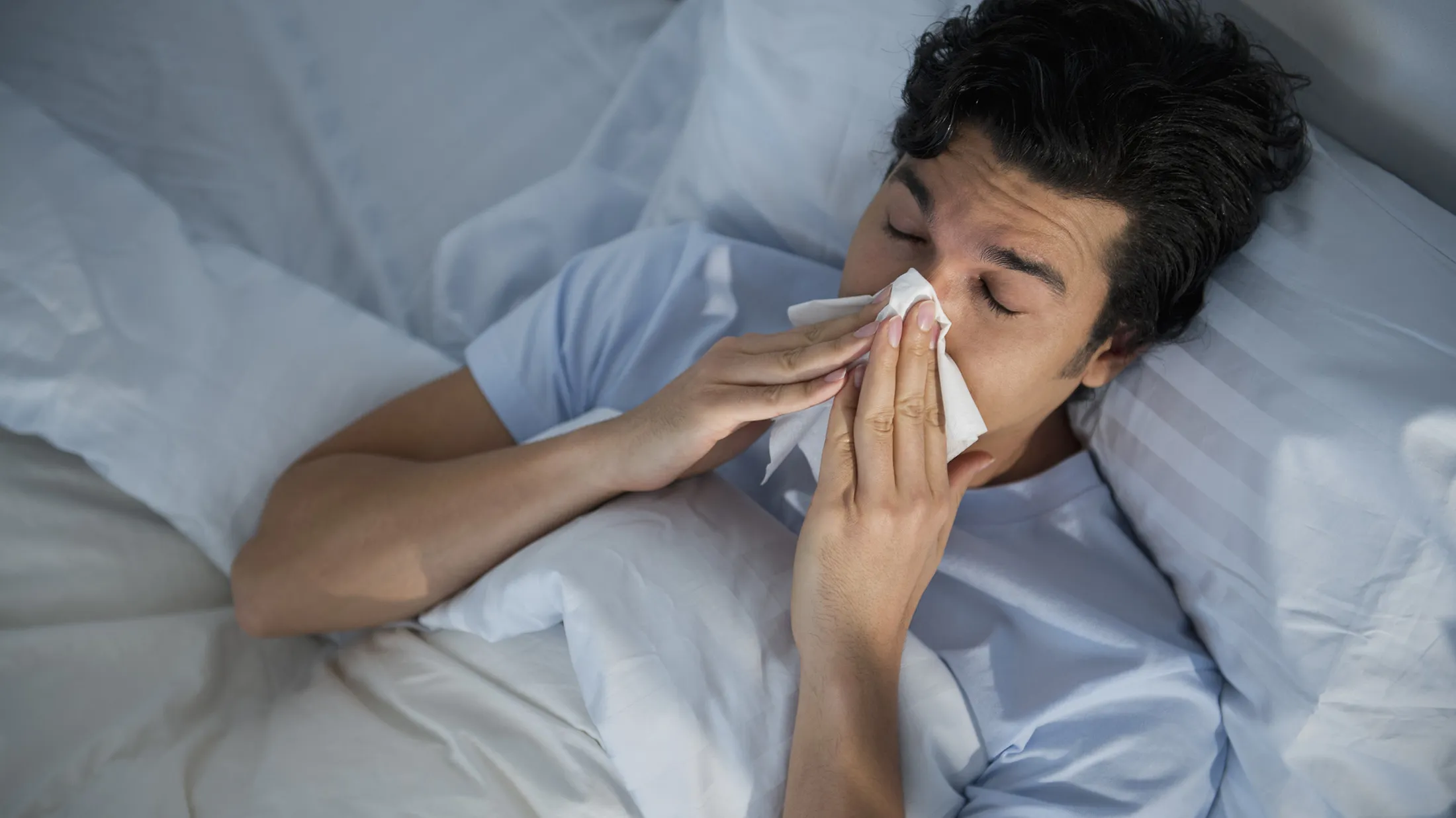 USA, New Jersey, Jersey City, man lying in bed and blowing nose