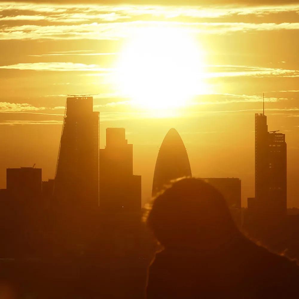 Onlookers watch the evening sun set on the horizon beyond skyscrapers including the Leadenhall building, also known as the 'Cheesegrater.'
