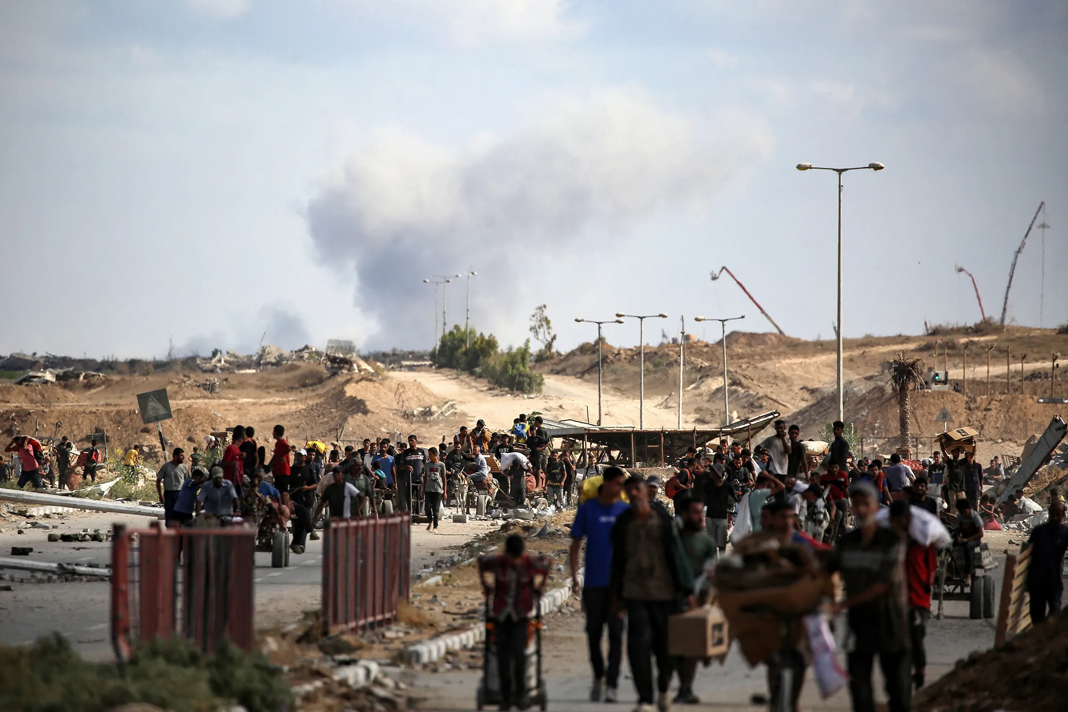 A plume of smoke rises as Palestinians return from a food distribution point near the Netsarim corridor in the Gaza Strip on Oct. 5.