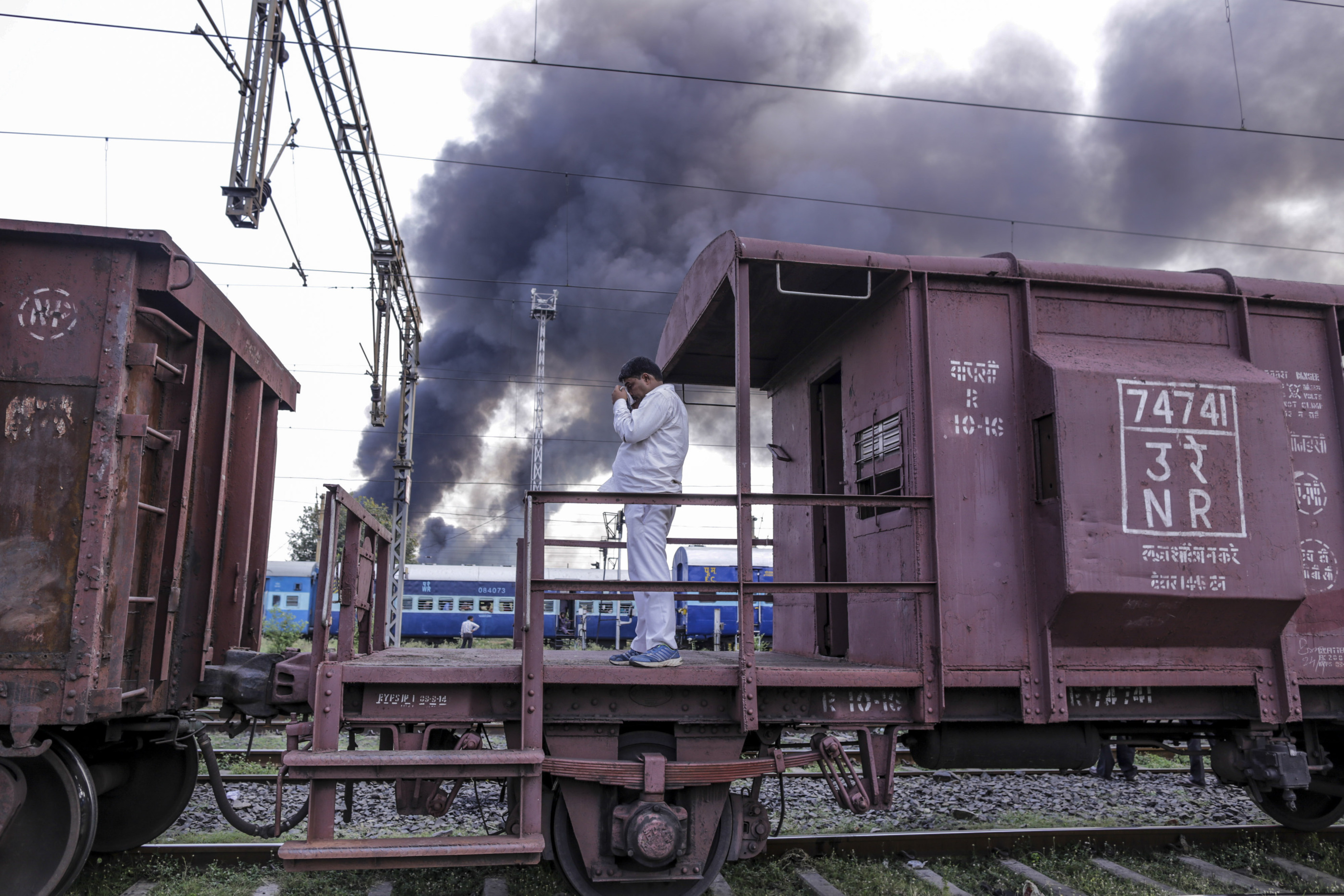 A railway employee stands on frieght train as smoke comes out from fire at the rail yard at Mughalsarai Rail Junction in Mughalsarai, India.