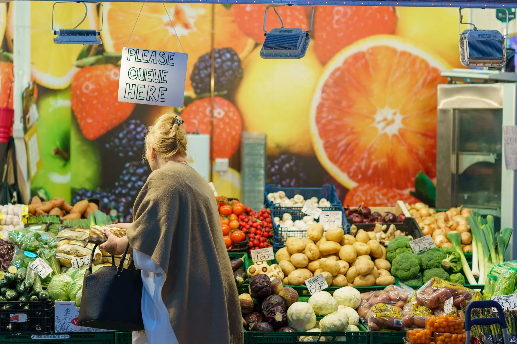 A shopper browses fruit and vegetables for sale at an indoor market in Sheffield, UK.