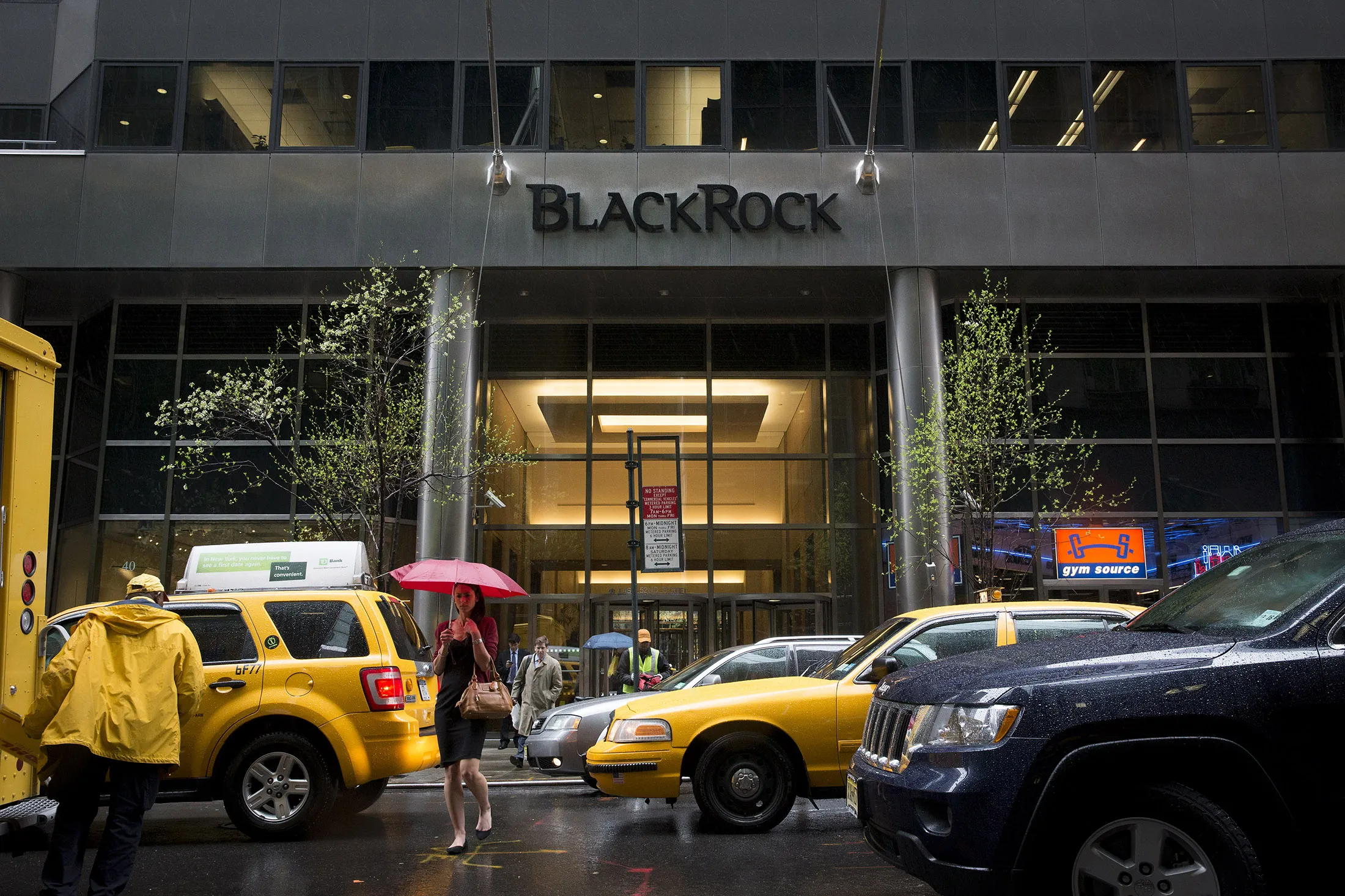 Pedestrians walking with umbrellas pass by taxi in front of BlackRock Inc. offices in New York, U.S., on Friday, April 12, 2013. BlackRock Inc. predicts Canadian 10-year benchmark bond yields may fall to the lowest since at least the 1950s as a sputtering economy douses expectations the Bank of Canada will increase borrowing costs this year.
