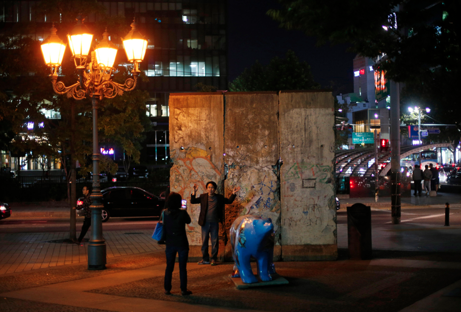 A woman takes a photograph of her husband in front of part of the Berlin Wall at Berlin square in Seoul October 17, 2014