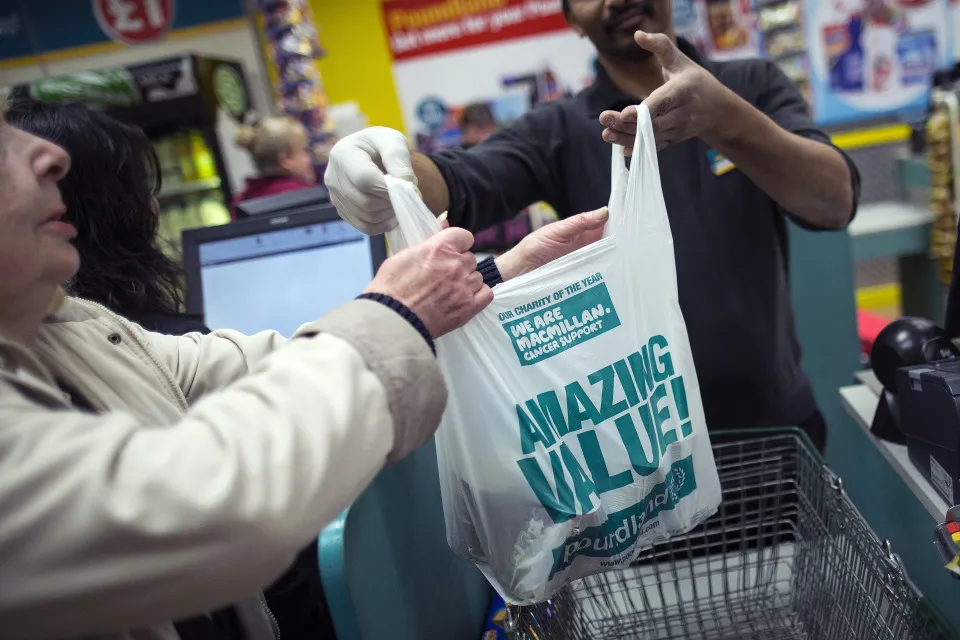 An employee hands a customer a plastic shopping bag at&nbsp;a Poundland&nbsp;store&nbsp;in London.
