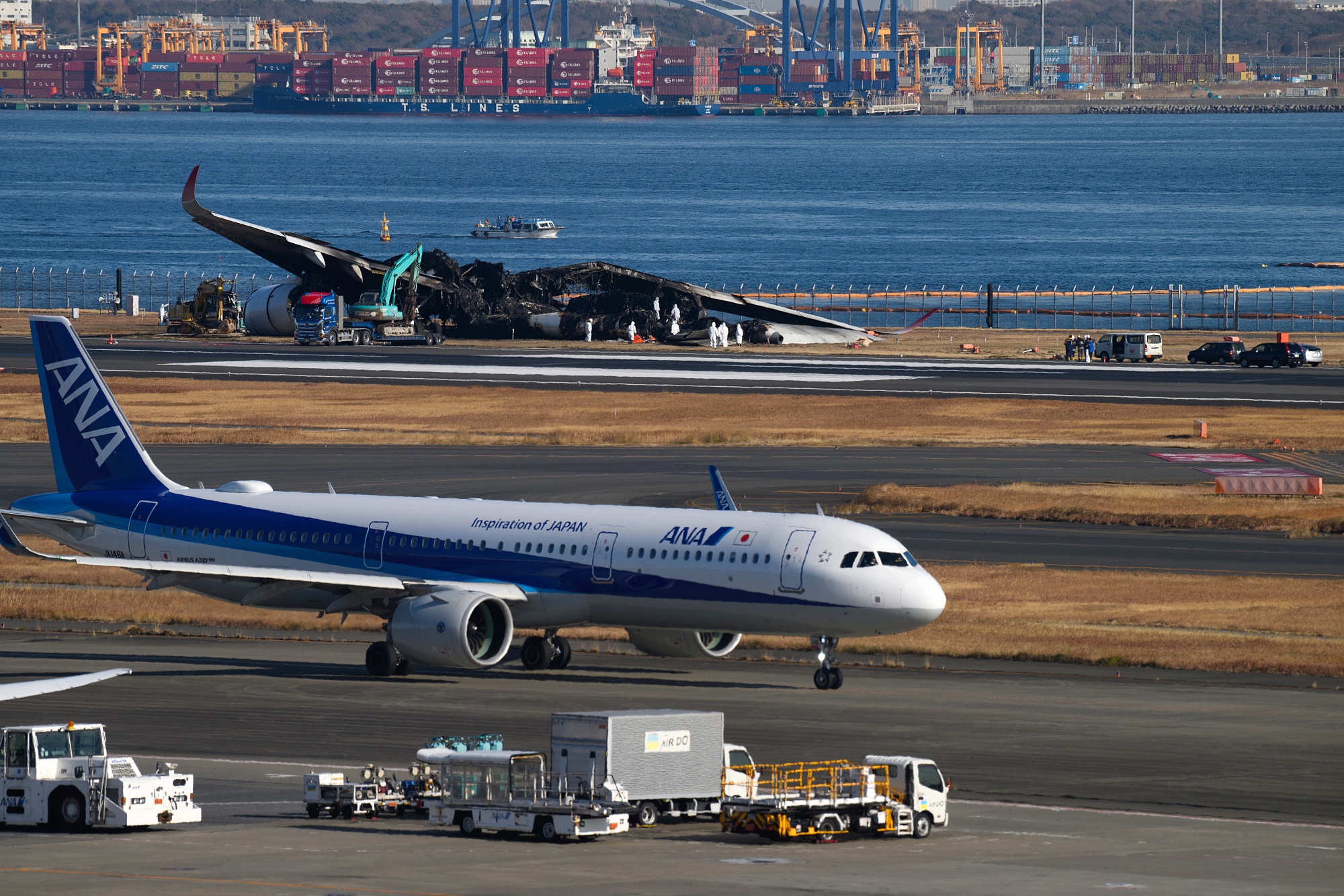 An aircraft past the wreckage of a Japan Airlines Co. passenger jet that collided Jan. 2 at Haneda Airport in Tokyo.