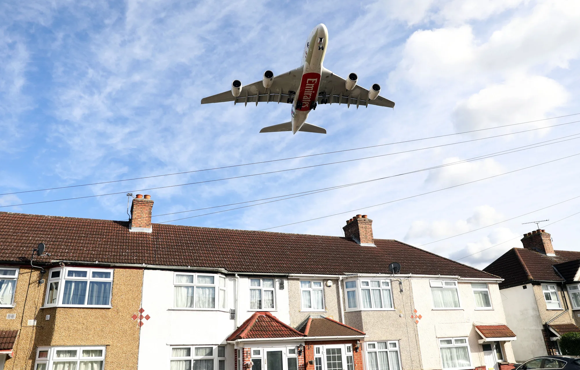A passenger aircraft operated by Emirates Airlines passes rooftops of residential houses as it prepares to land&nbsp;in London.