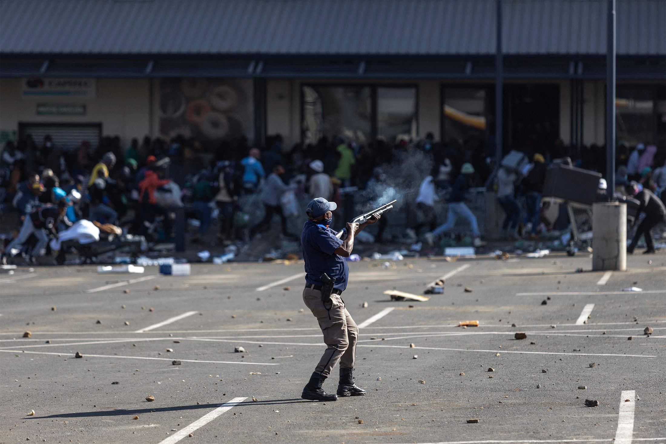 TOPSHOT - A member of the South African Police Services (SAPS) fires rubber bullets at rioters looting the Jabulani Mall in Soweto, southwest of Johannesburg, on July 12, 2021. - South Africa said it was deploying troops to two provinces, including Johannesburg, after unrest sparked by the jailing of ex-president Jacob Zuma led to six deaths and widespread looting. Overwhelmed police are facing mobs who have ransacked stores. Six people have died, some with gunshot wounds, and 219 people have been arrested, according to a police tally issued before the army deployed. (Photo by GUILLEM SARTORIO / AFP) (Photo by GUILLEM SARTORIO/AFP via Getty Images) Photographer: Gillem Sartorio/AFP/Getty Images