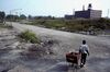 Another man in a blue baseball cap with a shopping cart rounding the same corner; this time, most the of the metal and tires are gone and some factories demolished