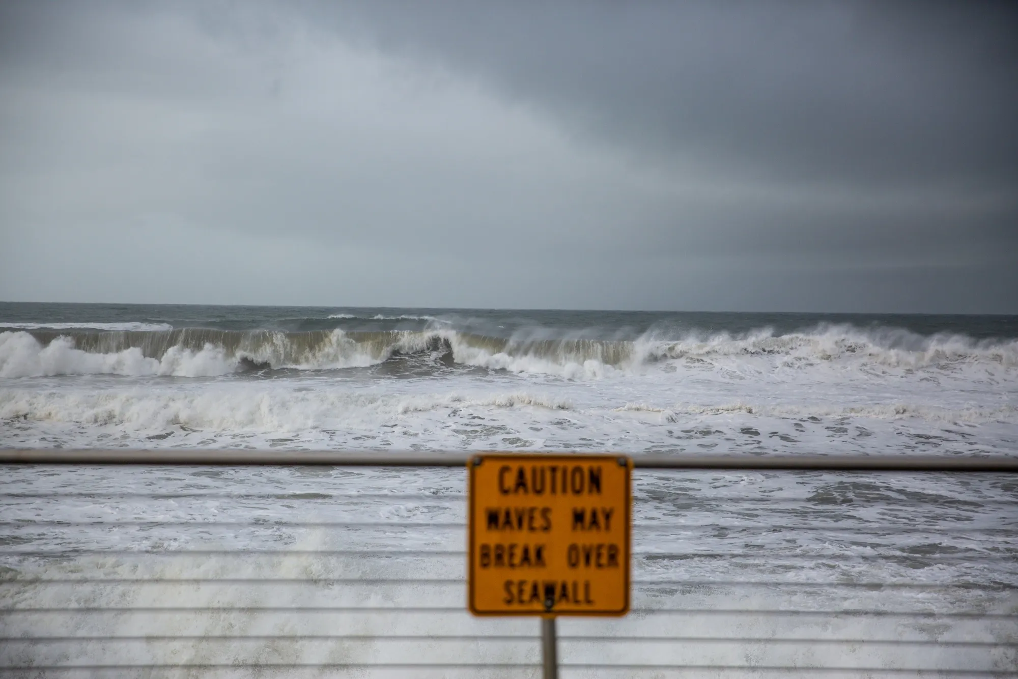 Waves Break Beyond A Warning Sign On A Seawall