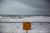 Waves Break Beyond A Warning Sign On A Seawall