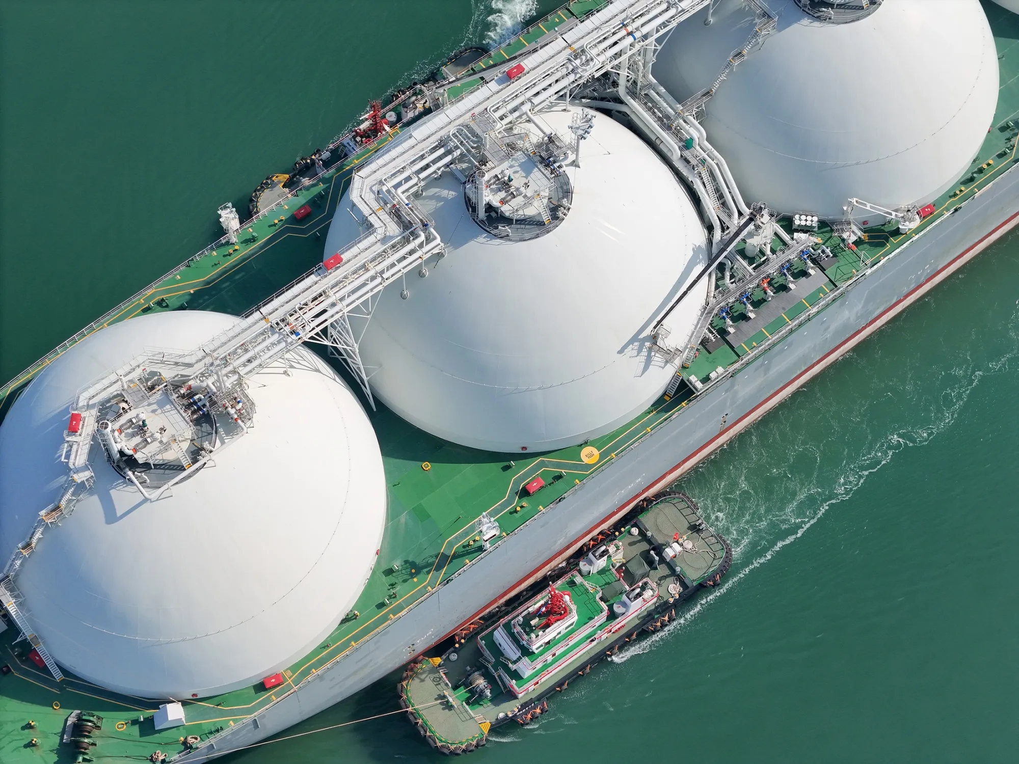 A large LNG (liquefied natural gas) transport ship with three visible storage domes is assisted by a tugboat as it docks in Yantai, China last month.