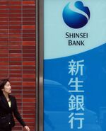 A pedestrian walks past a sign for Shinsei Bank Ltd. outside one of their branches in Tokyo, Japan.
