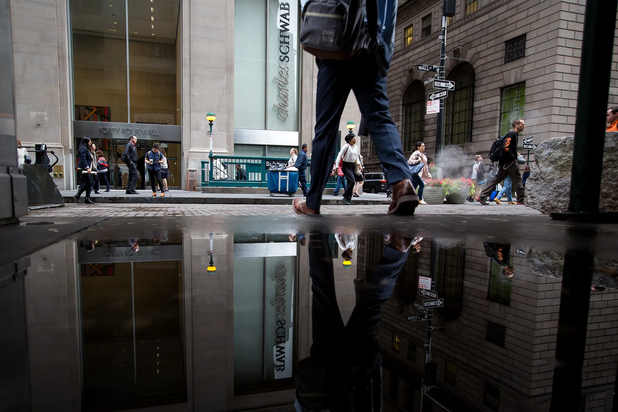 Pedestrians pass in front of a Charles Schwab Corp. branch on Wall Street near the New York Stock Exchange.