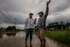 Wilson Castro, left, an opposition activist, speaks with a resident while standing barefoot on flooded road. Photographer: Meredith Kohut/Bloomberg
