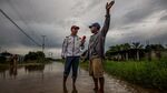 Wilson Castro, left, an opposition activist, speaks with a resident while standing barefoot on flooded road. Photographer: Meredith Kohut/Bloomberg
