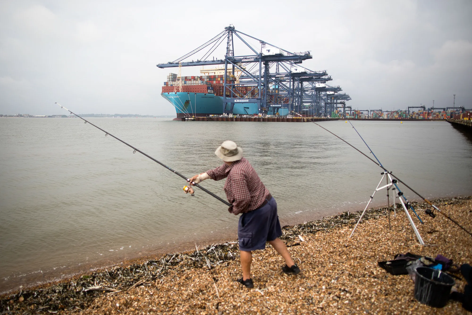 A man casts a fishing rod as a container ship sits at the Port of Felixstowe.