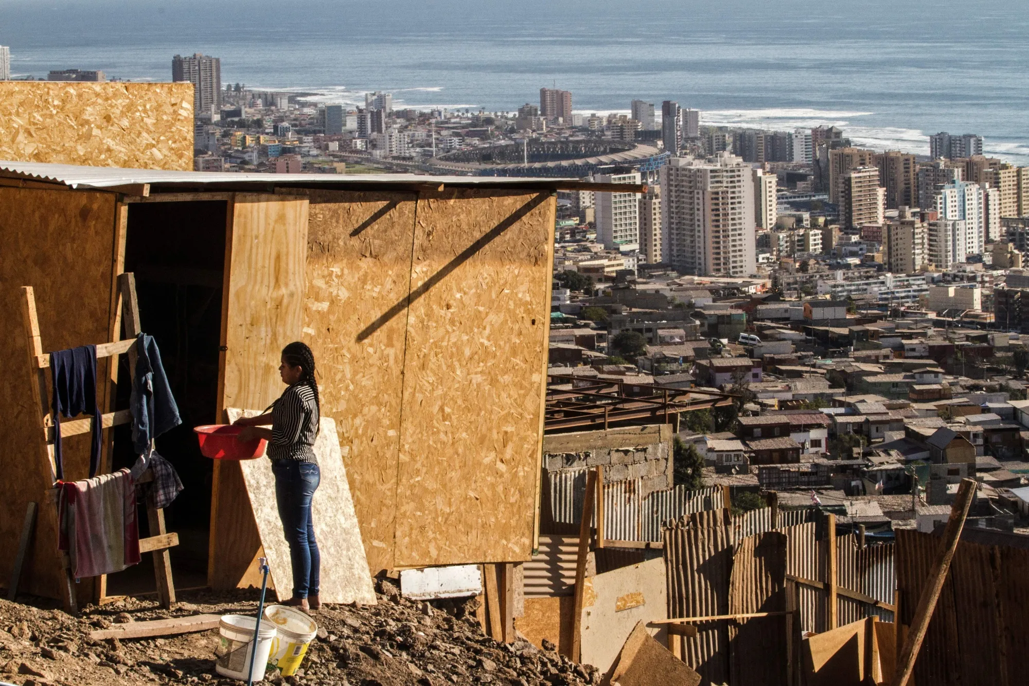 A woman stands outside her house at an informal&nbsp;camp in Altamira, Chile, with the city of Antofagasta in the background.&nbsp;
