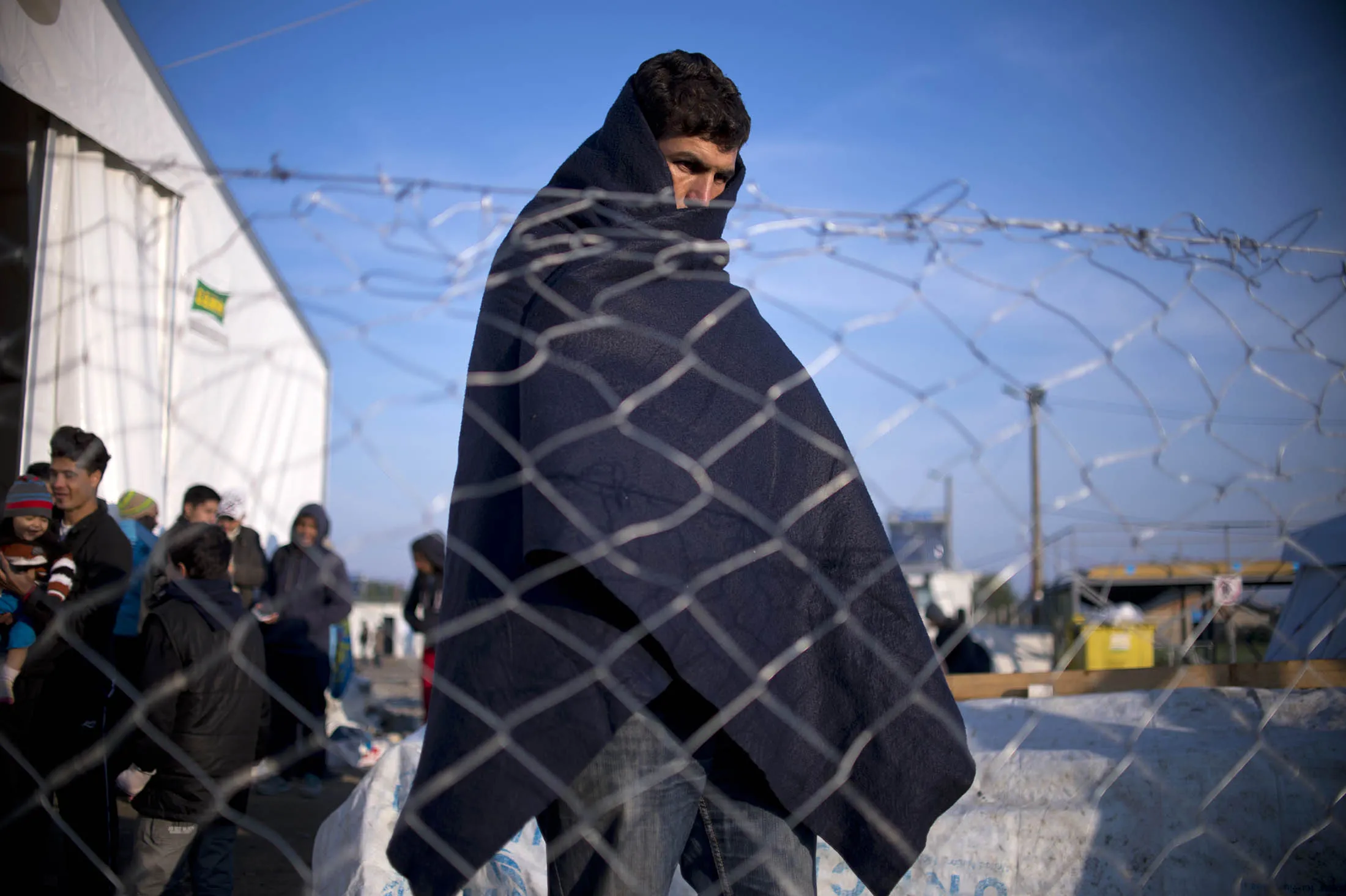 A migrant wearing a blanket to warm himself, waits in a registration camp in Macedonia .
