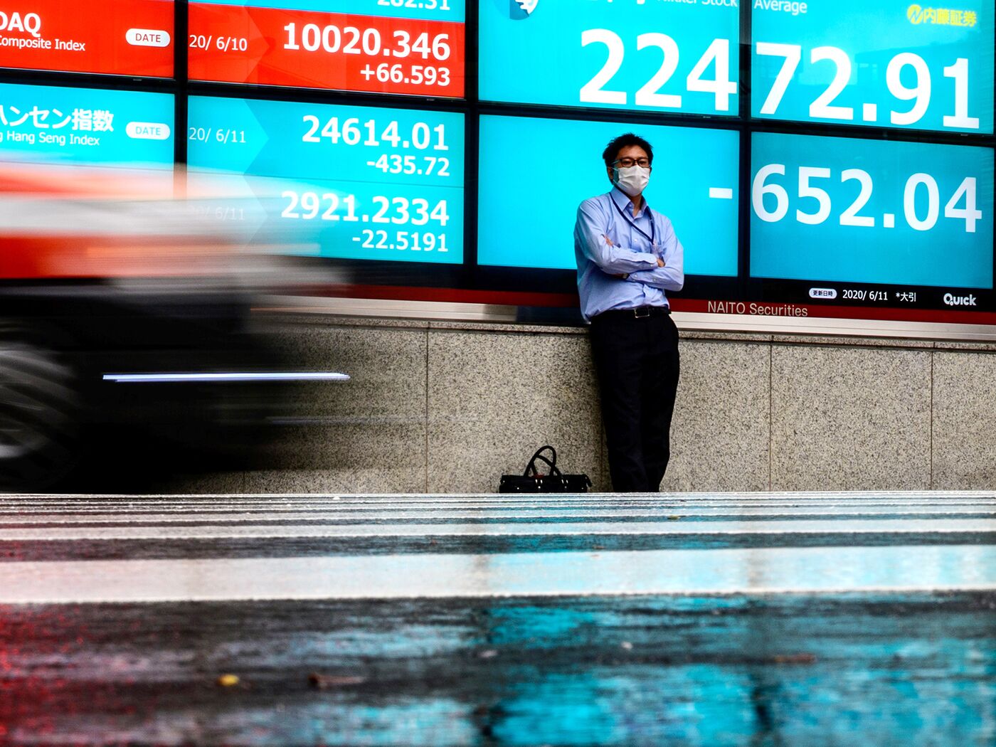 A man wearing a face mask stands in front of an electric quotation board displaying the numbers of the Nikkei 225 Index on the Tokyo Stock Exchange in Tokyo on June 11, 2020.