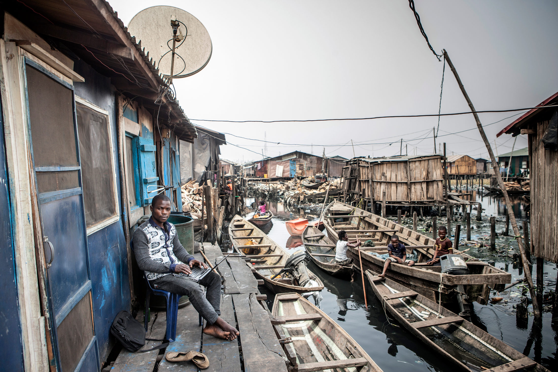 Zoology student Samuel Pelumi works on his laptop outside his home alongside the Lagos Lagoon.
