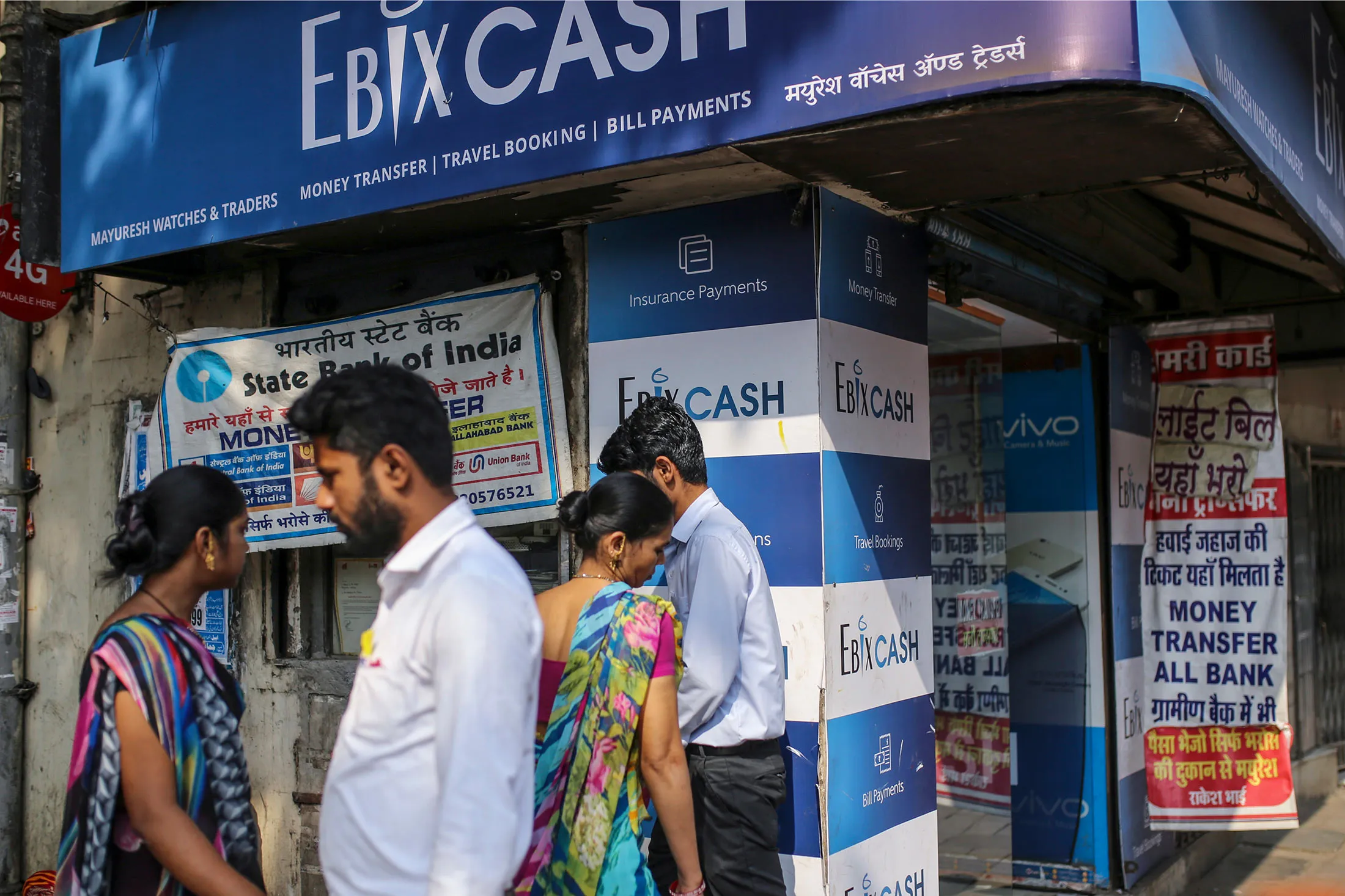 Pedestrians pass&nbsp;an&nbsp;EbixCash logo outside Rakesh Sharma’s Mayuresh Watches and Trader shop&nbsp;in the&nbsp;Byculla area of Mumbai,&nbsp;on Jan. 29, 2018.&nbsp;