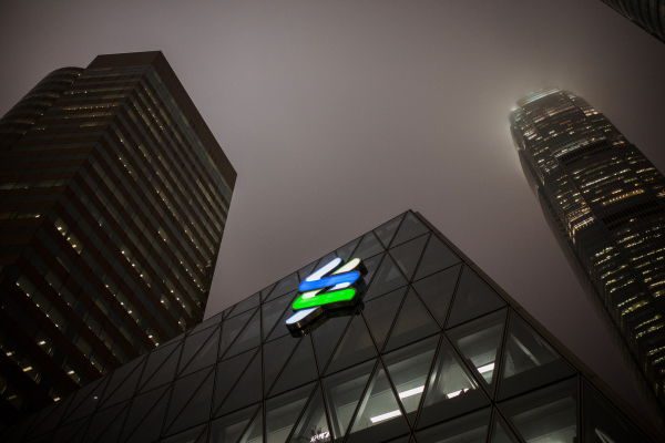 The Standard Chartered Plc logo is illuminated at night atop the company's offices at the Forum building in the Central district of Hong Kong.