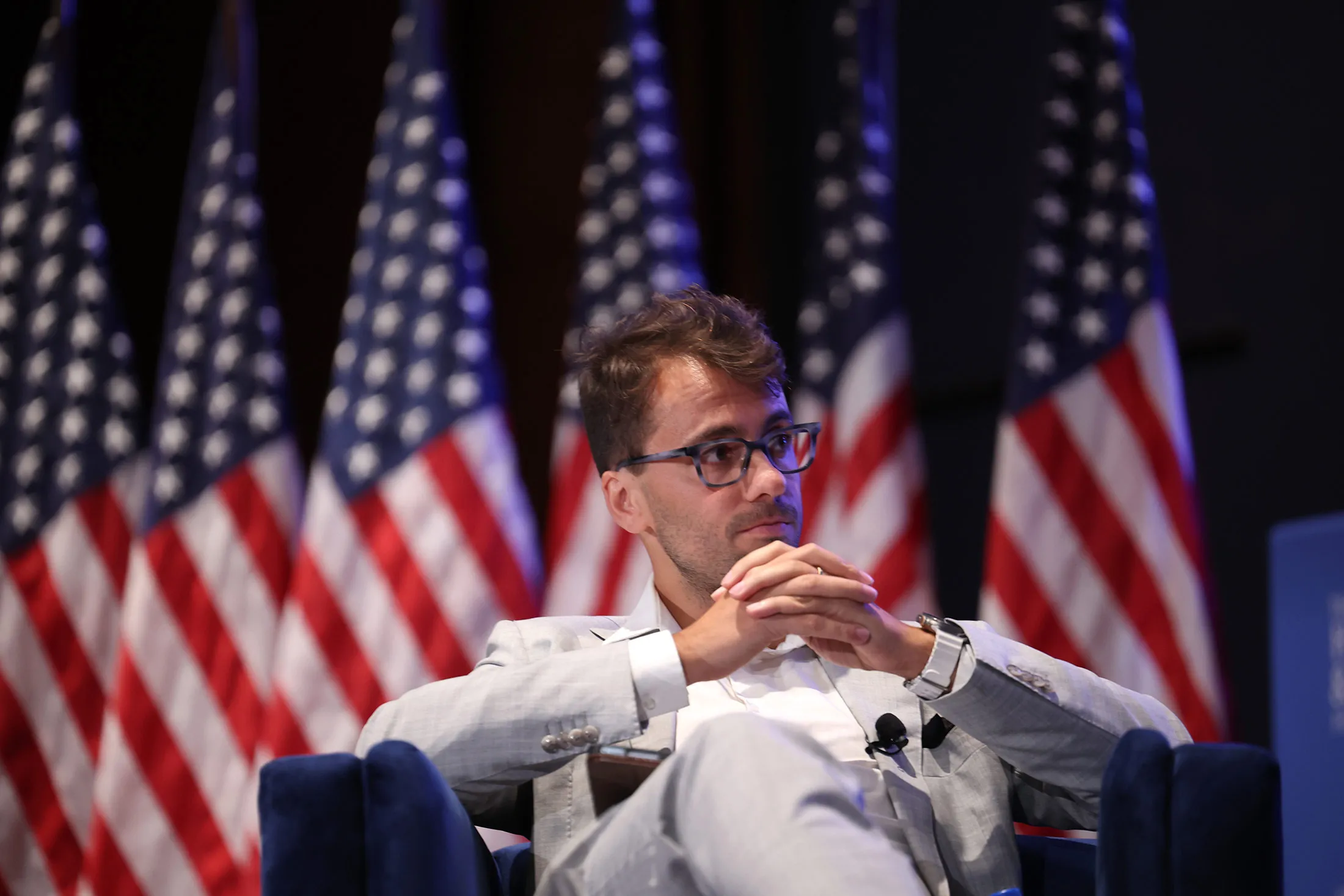 Delian Asparouhov sits in a chair on a stage with American flags behind him