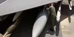 A technician inspects the fuel tank on the wing of a fighter jet. 