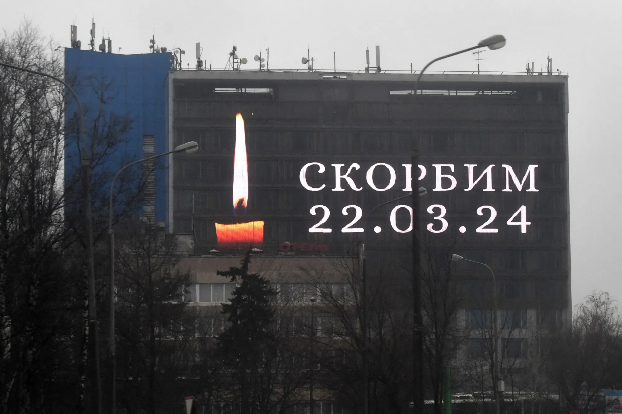 An advertising screen on a building displays an image of a lit candle and the slogan "(We) Mourn" in memory of victims of the concert hall gun attack in Moscow.