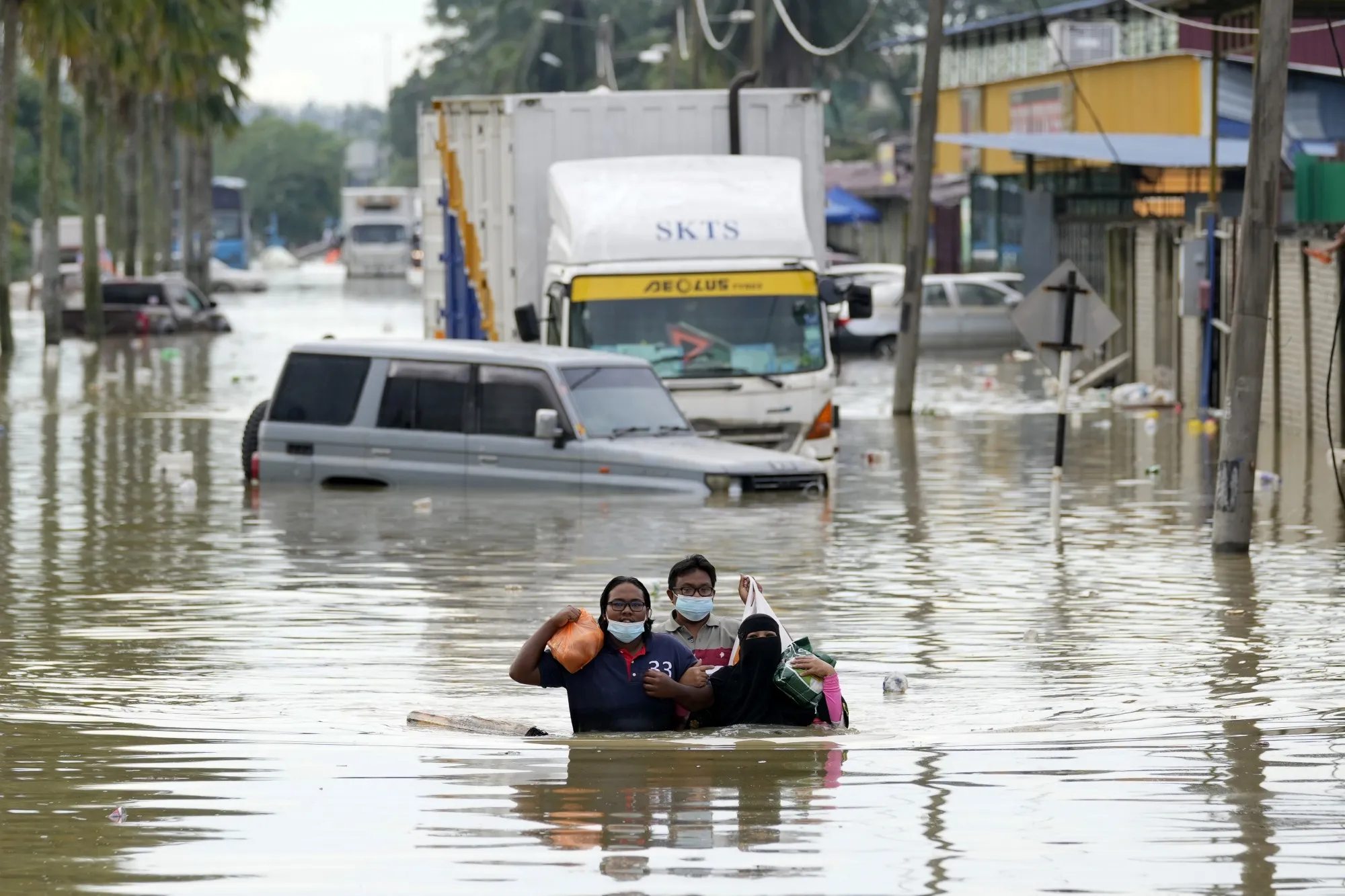 Residents wade through a flooded road in Shah Alam, on the outskirts of Kuala Lumpur, Malaysia, Monday, Dec. 20, 2021. Rescue services on Monday worked to free thousands of people trapped by Malaysia's worst flooding in years after heavy rains stopped following more than three days of torrential downpours in the capital and around the country. (AP Photo/Vincent Thian)