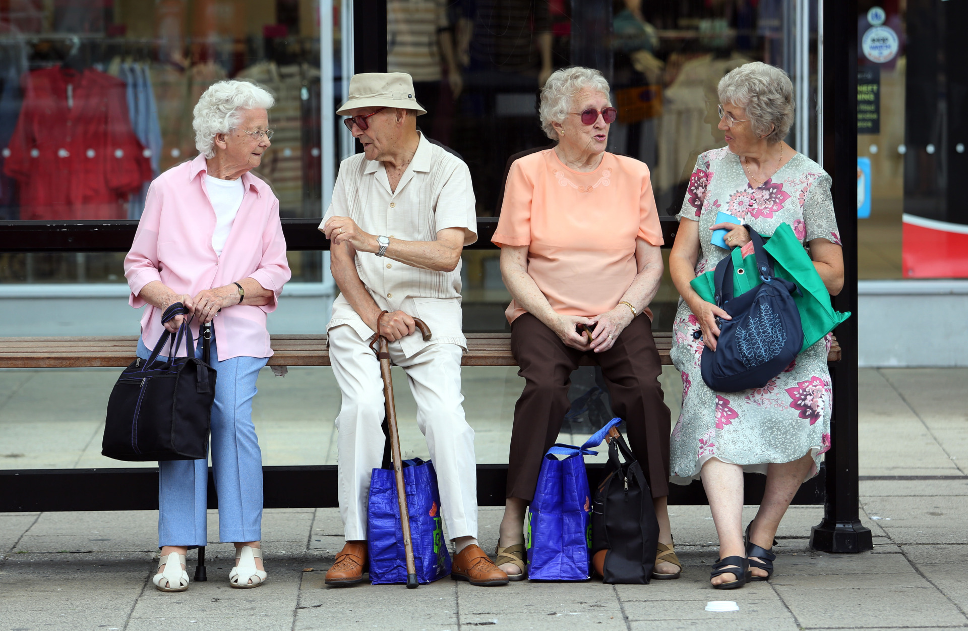 Elderly people sit with their shopping bags as they wait for transportation at a bus stop in Hastings, UK, on Tues., July 23, 2013.
