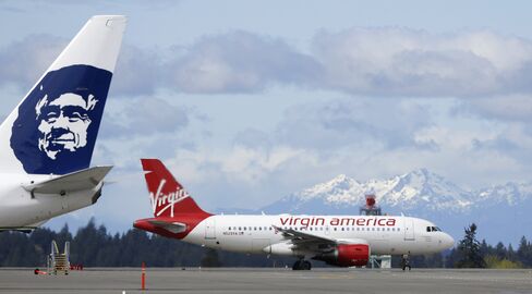 A Virgin America plane taxis past an Alaska Airlines plane waiting at a gate at Seattle-Tacoma International Airport.