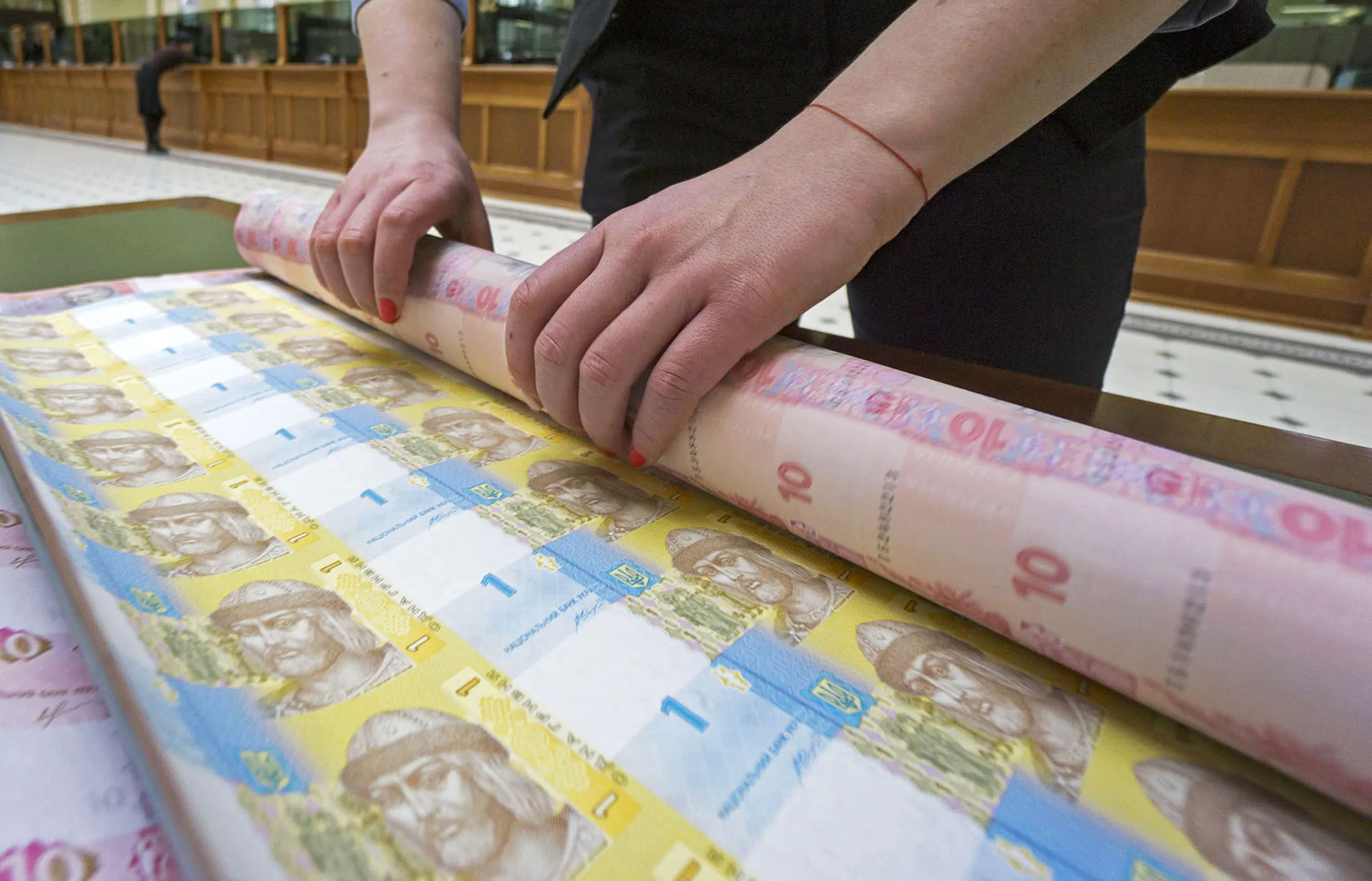 A bank worker rolls up uncut sheets of ten and one hryvnia banknotes after arranging for a photograph at the headquarters of the National Bank of Ukraine in Kiev, Ukraine, on Tuesday, March 22, 2016. Ukraine's political gridlock, already holding up billions of dollars in aid, is also threatening financial stability and postponing monetary easing, according to the nations central bank governor.
