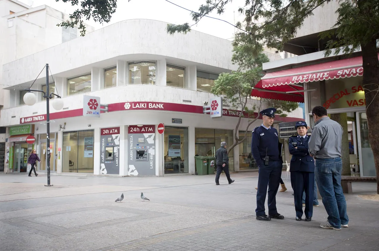 Police officers at a branh of Cyprus Popular Bank Pcl, also known as Laiki Bank, as banks open for the first time in two weeks in Nicosia, Cyprus, on March 28, 2013. The Central Bank of Cyprus's capital controls included a 300-euro ($383) daily limit on withdrawals and restrictions on transfers to accounts outside the country. Photographer: Simon Dawson/Bloomberg