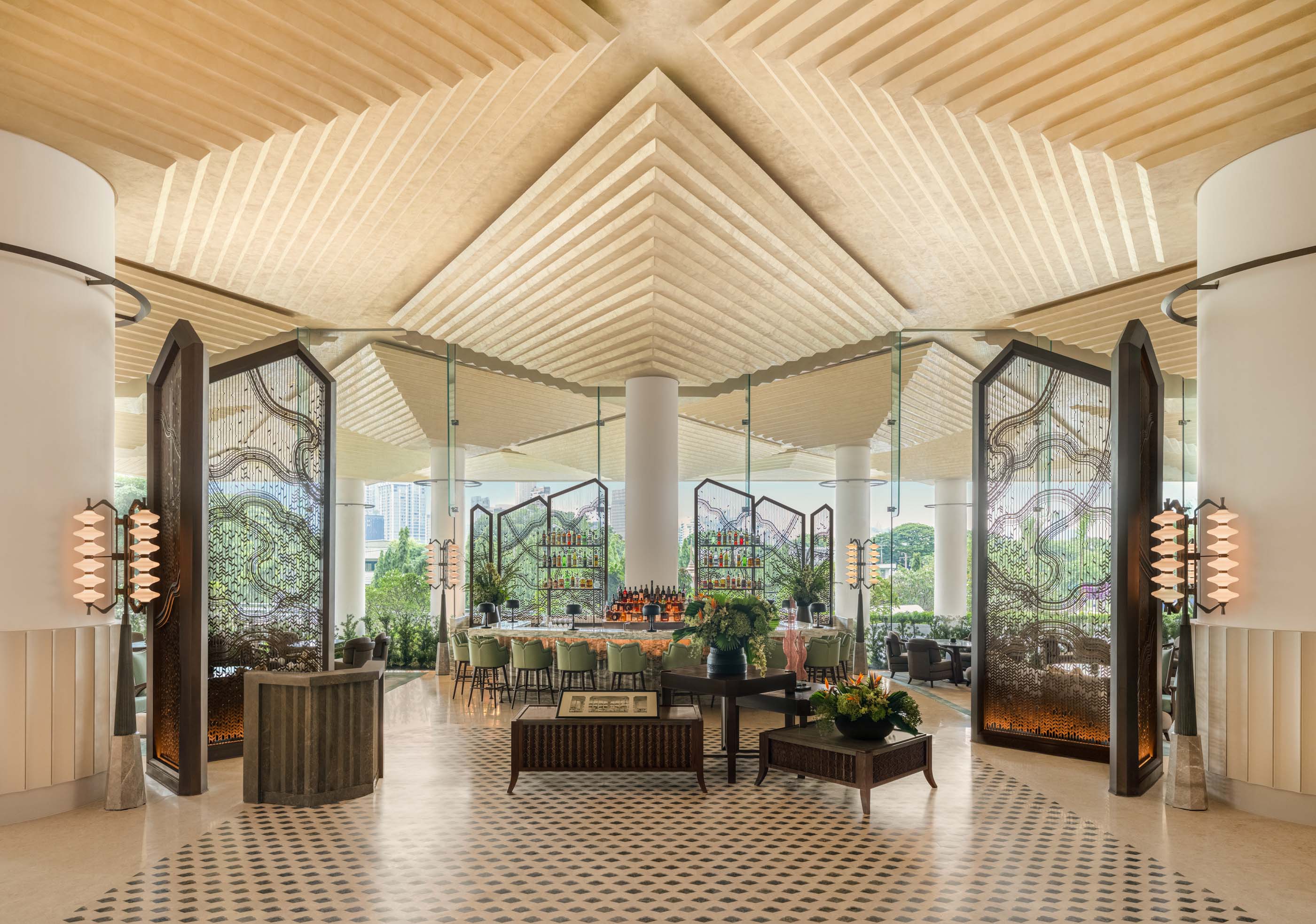 A geometric ceiling and intricate metal screens define the grand lobby bar at Dusit Thani Bangkok.