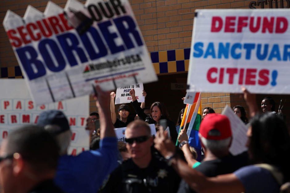 Protesters in California raise signs criticizing the sanctuary movement
