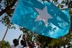 A Somali man holds a Somali flag while o