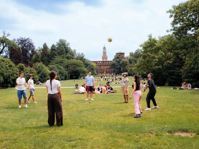 A group of people toss a volleyball around on a lawn in the Parco Sempione.