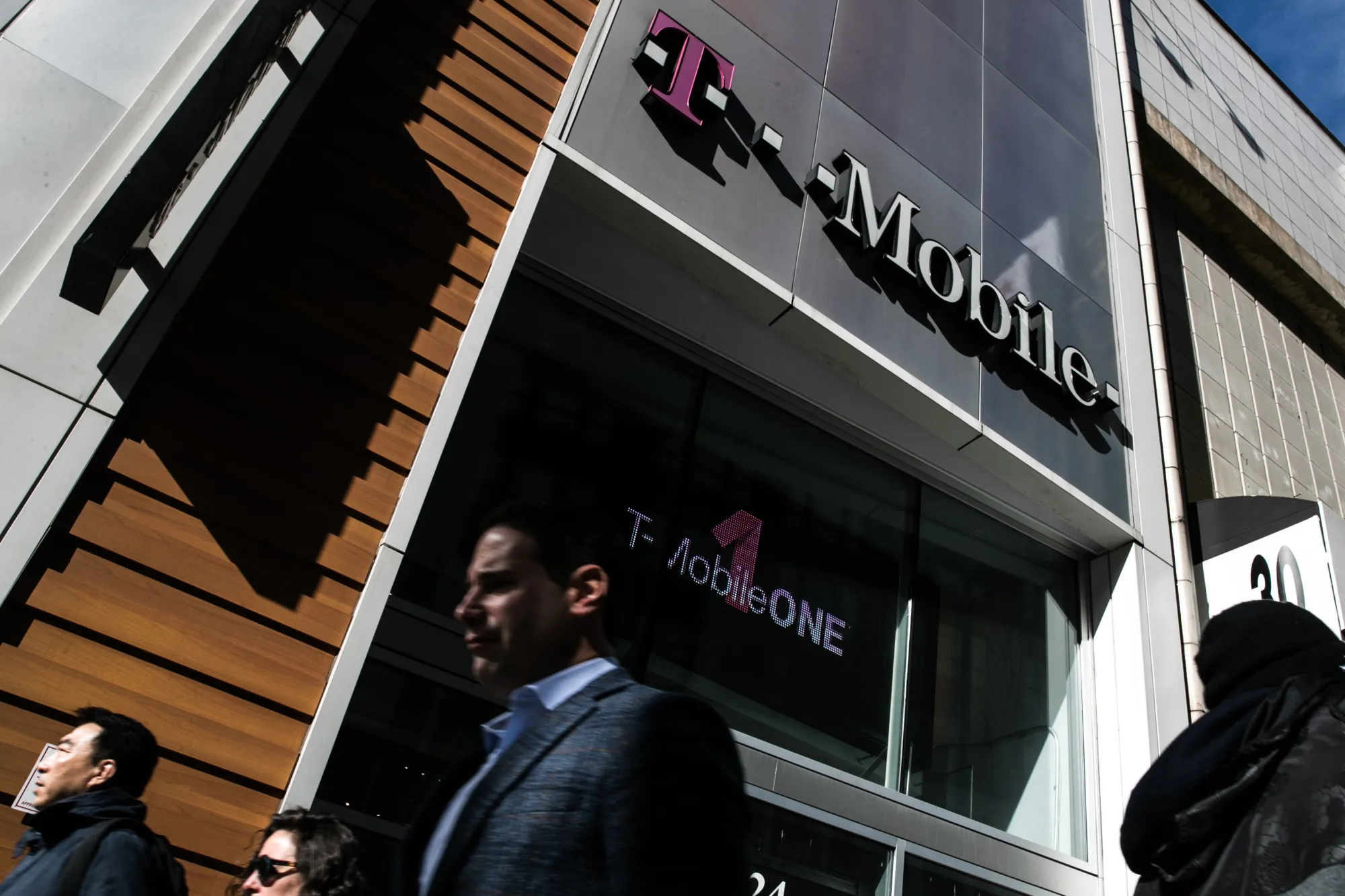 Pedestrians pass in front of a T-Mobile US Inc. store in New York.