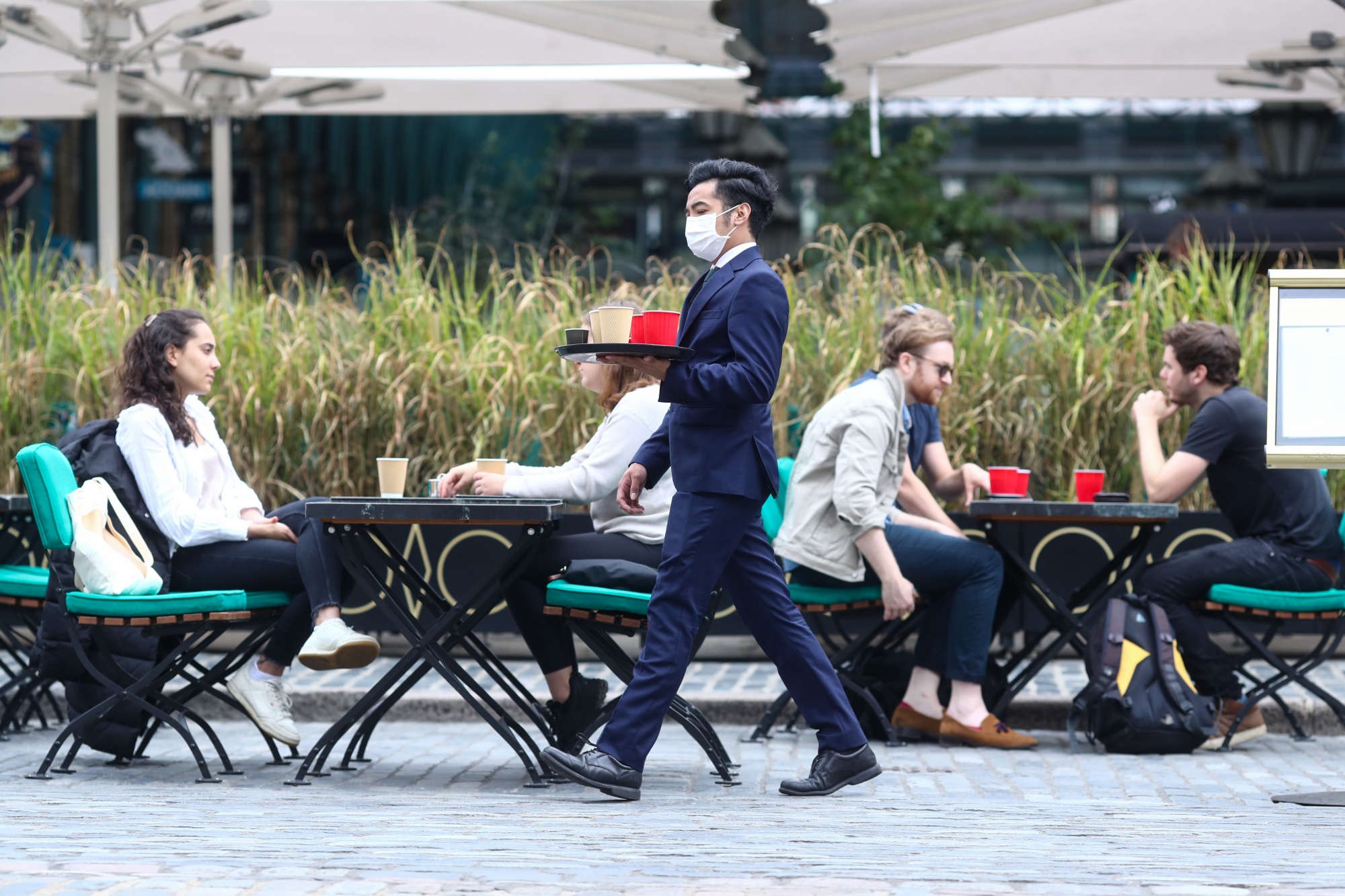 A waiter wearing a protective face mask serves customers sitting at a cafe's terrace in&nbsp;London.
