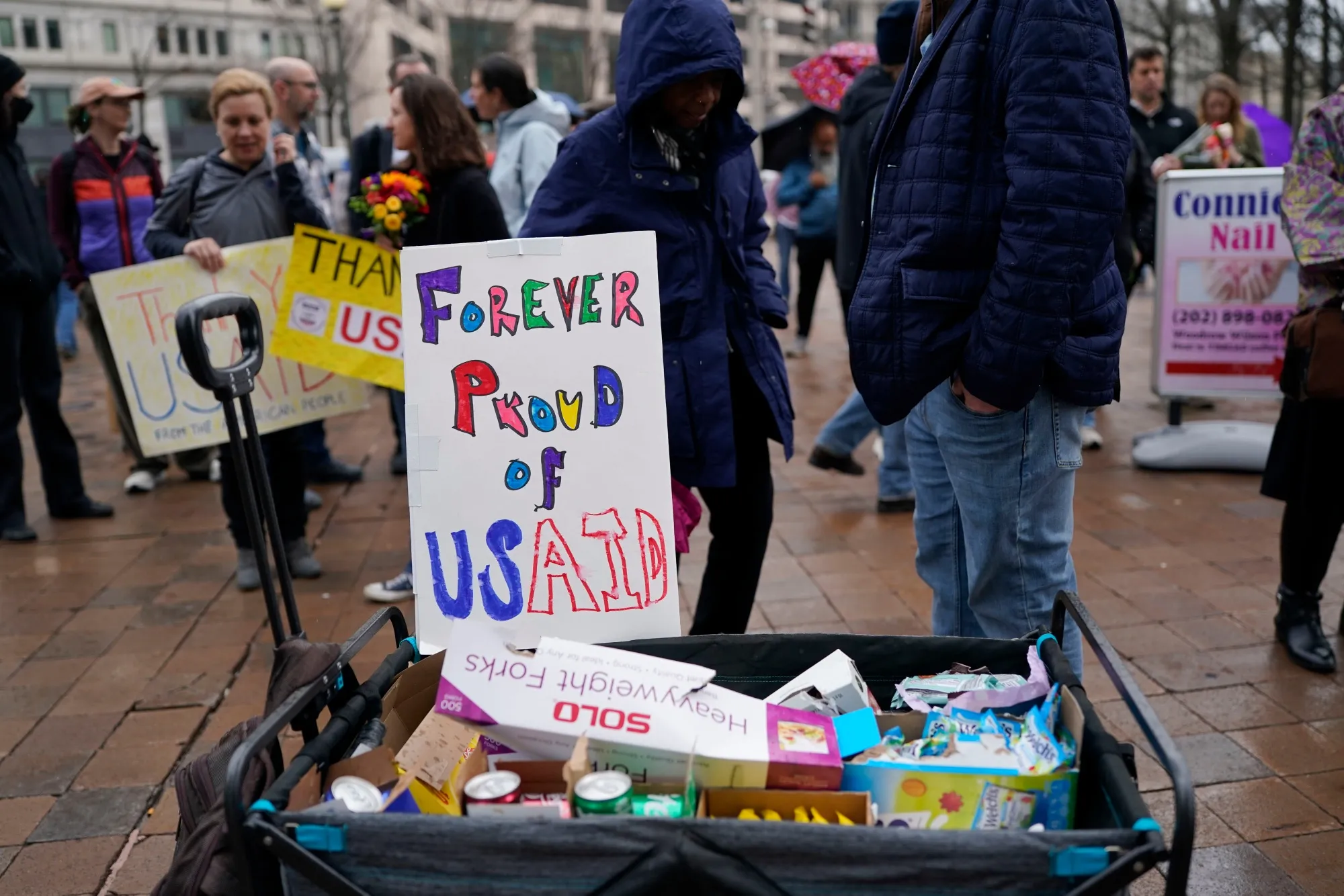 Demonstrators display a sign and offer supplies during a “clap out” in support of USAID&nbsp;workers on Feb. 27.