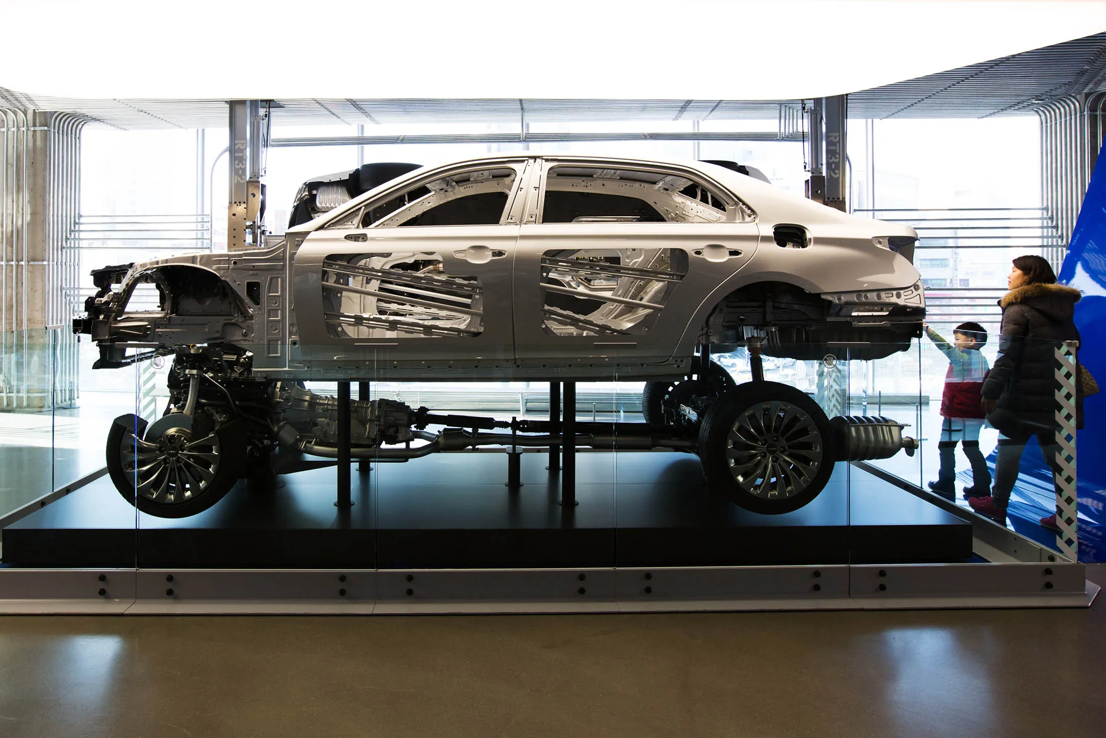 Customers look at the frame and chassis of a Hyundai Genesis G90 luxury sedan.
