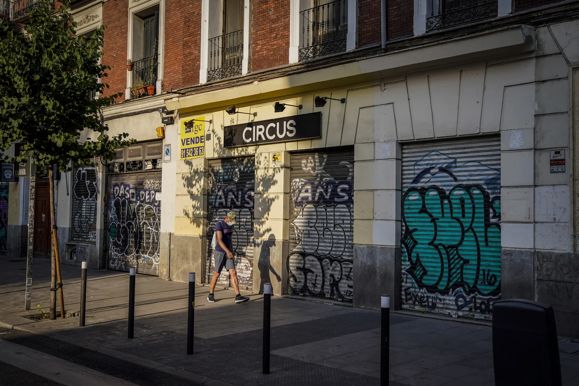 A pedestrian walks past the closed shutters of businesses in Madrid.