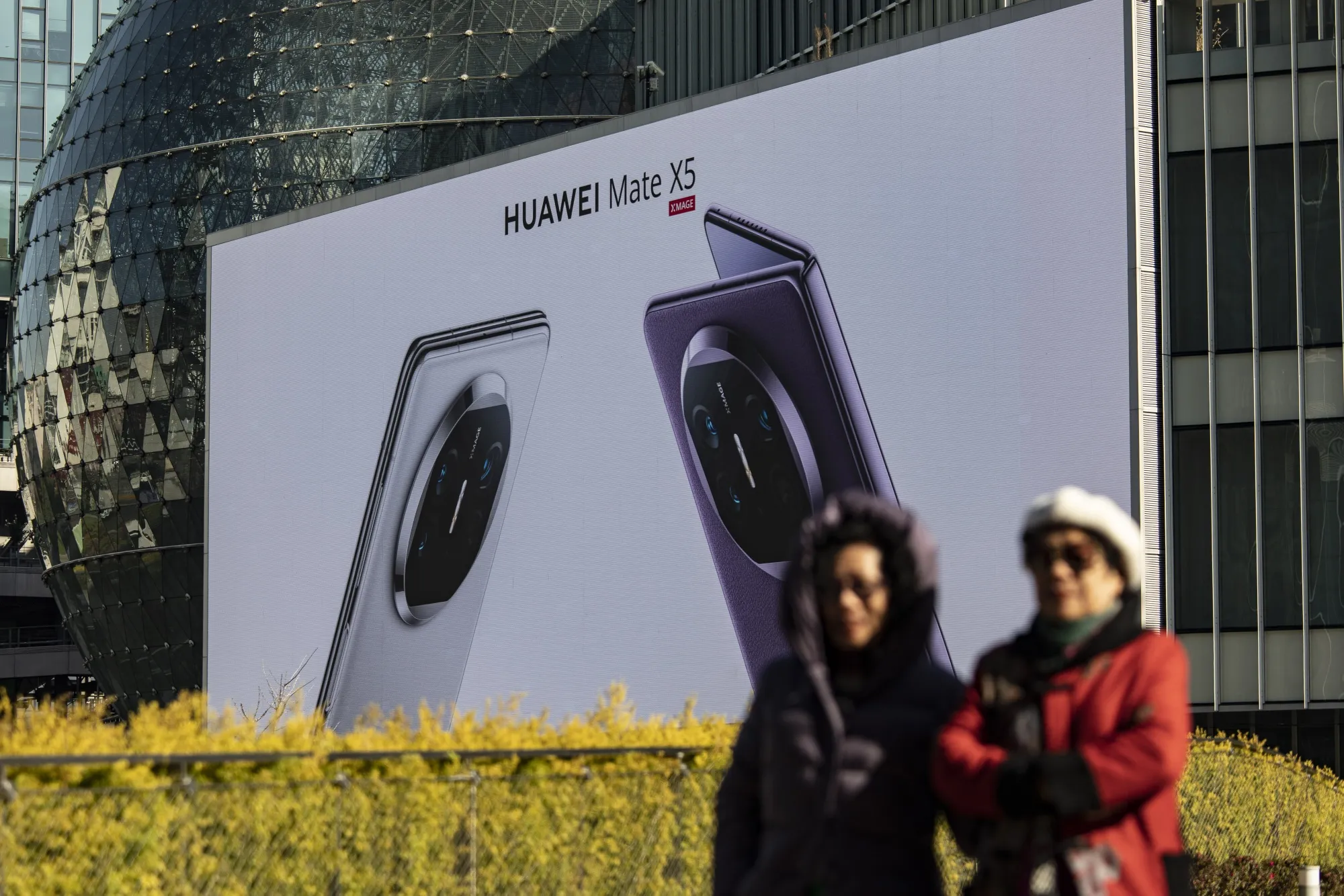 Pedestrians pass&nbsp;a large advertisement for Huawei phones in Shanghai.