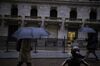 Pedestrians carry umbrellas while walking along Wall Street in front of the "Fearless Girl" statue in New York, U.S., on Thursday, Jan. 24, 2019. While the three major U.S. equity benchmarks gained on Friday, it wasn’t enough to keep a string of four weekly advances above 1.5 percent alive.