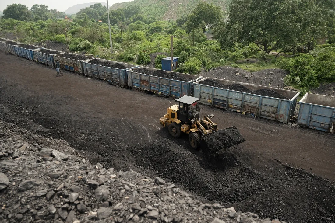 A worker operates a wheel loader to move raw coal into train carriages on the outskirts of Dhanbad, India.
