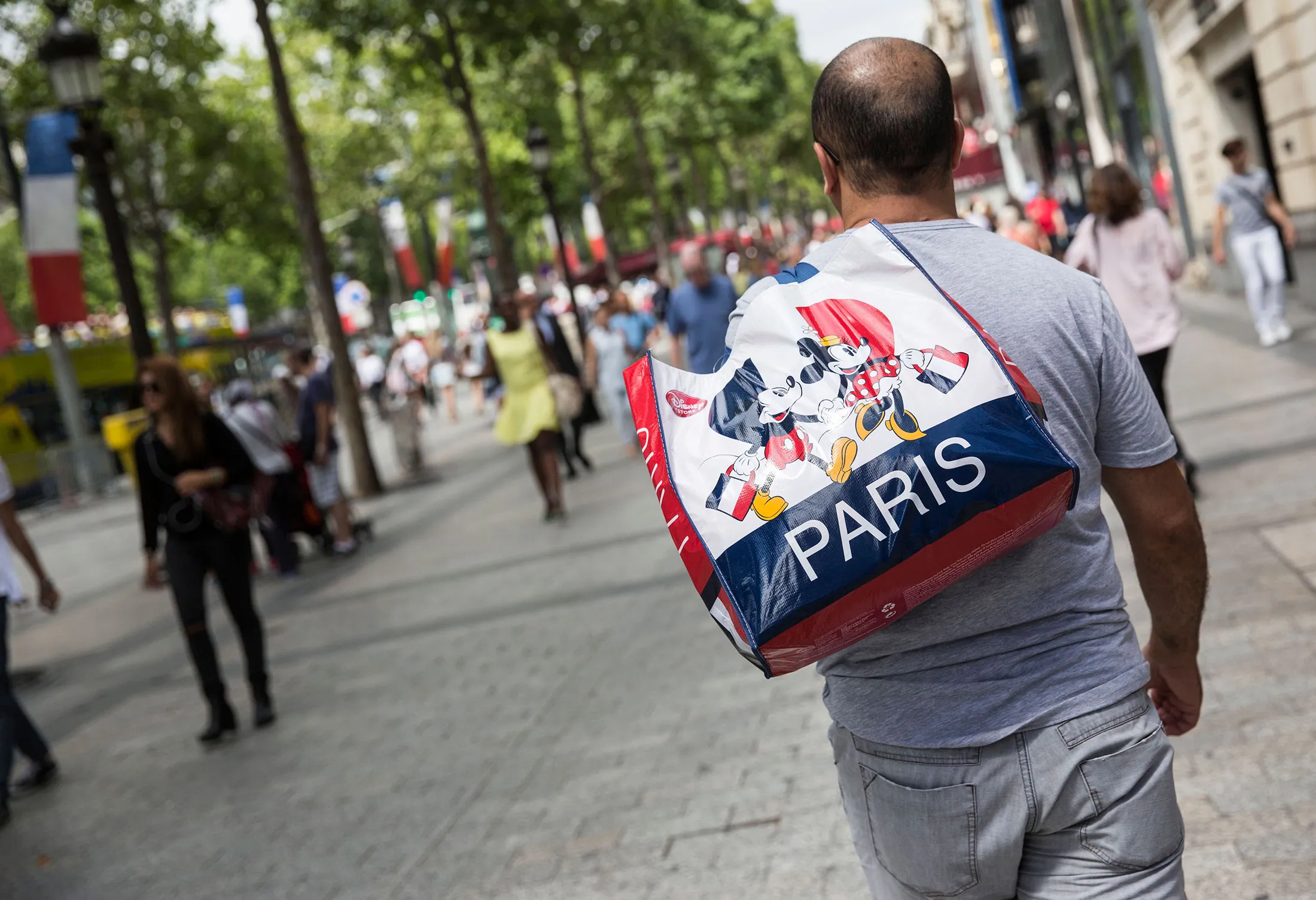 A shopper carries a Disney Store branded carrier bag on the Avenue des Champs-Elysee in Paris, France, on Tuesday, July 21, 2015. The French Competition Authority has acquired new powers to streamline merger control, dilute retail dominance, control the establishment of regulated legal professions and the fees they charge.
